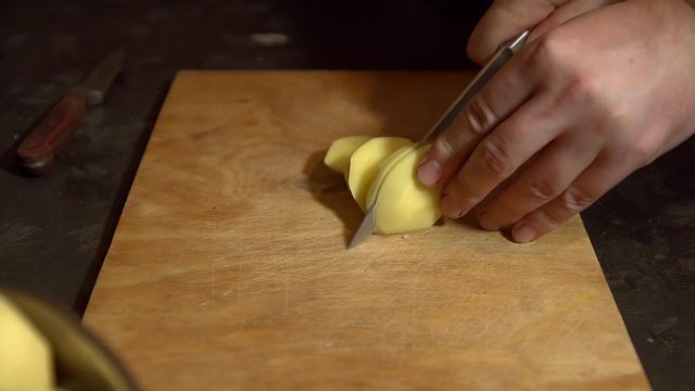 Tuber of potato is cut manually with a knife into pieces. On a wooden Board with a knife cut the vegetable. Potatoes prepared for frying. Smooth the potato slices are on the Board.