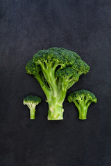 Three green broccoli on dark gray slate background