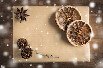 Vintage Christmas Kraft Gift Box in Rustic Style Decorated with Cones and Dried Orange Slices. Snow Falling Effect.