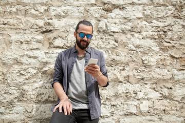 man texting message on smartphone at stone wall