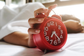 Irritated young woman putting her alarm clock off in the morning with soft morning light. Relaxing concept..