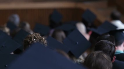 Many young people in academic hats sitting at assembly hall, graduation ceremony
