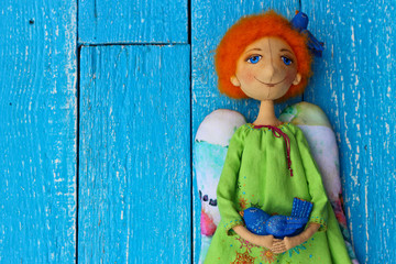 Obraz na płótnie Canvas Angel with ginger hair green embroidered patterned shirt and a blue bird in the hand. Textile handmade doll.