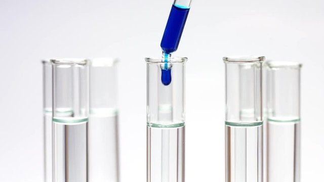 Close up of drop blue liquid in test tubes with clean water rotating on white background