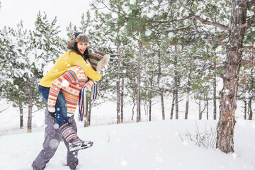 Loving couple in the winter park. Man and woman dressed in sweaters and scarves, winter hats. Snowfall in the forest, holidays, travel.