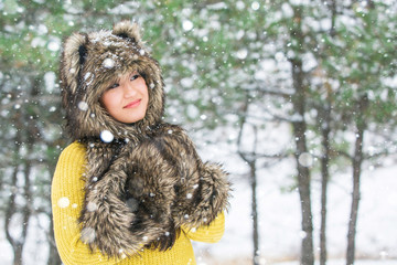 Portrait of a happy woman in a winter park. The girl wearing fur hat, mittens. Snowfall winter forest, trees in the snow. Copy space.
