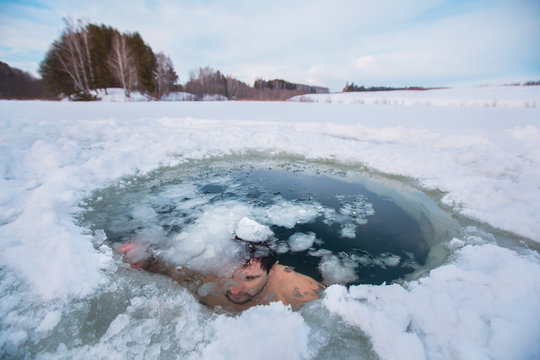 Young man swimming in the winter lake in the ice hole