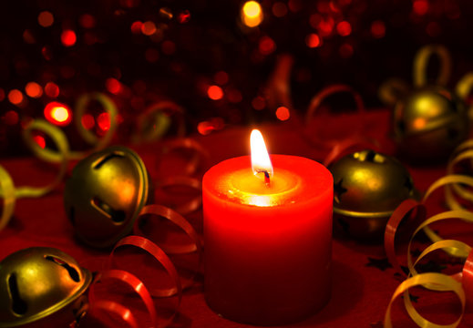 Christmas and New Year`s festive evening burning candle bokeh image. Greeting card  dark Background concept with holiday tinsel,jingles bells, twisted ribbons and copyspace place for text or logo.