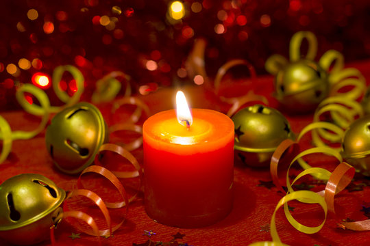 Christmas and New Year`s festive evening burning candle bokeh image. Greeting card  lights Background concept with holiday tinsel,jingles bells, twisted ribbons and copyspace place for text or logo.