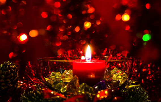 Christmas and New Year`s festive evening burning candle bokeh image. Greeting card  red lights Background concept with holiday colorful glass tinsel, and copyspace place for text or logo.