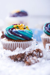 Winter cupcakes with gradient cream and golden stars on a snow with presents, cone and snowflakes on a background. Close view. Vertical shot.