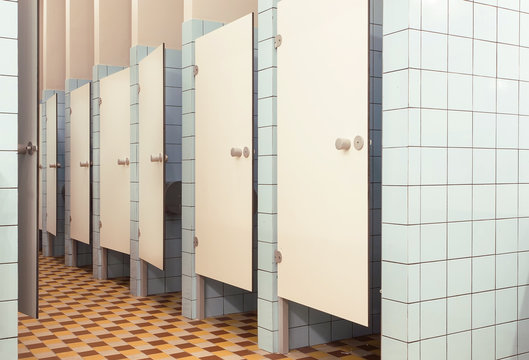 White doors in minimalistic interior of public bathroom with toilet booths