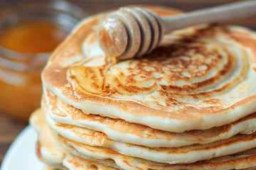 Stack of delicious, homemade pancakes with honey on white plate on wooden background. Healthy breakfast, close up. Pancake's Day. High stack of pancakes shallow DOF.