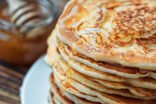 Stack of delicious, homemade pancakes with honey on white plate on wooden background. Healthy breakfast, close up. Pancake's Day. High stack of pancakes shallow DOF.