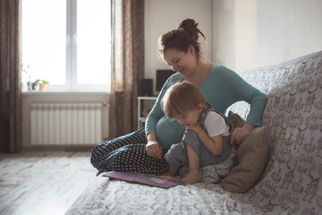 young pregnant mother and son reading a book on sofa, lifestyle,