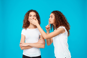 One of sisters twins showing keep silence over blue background.