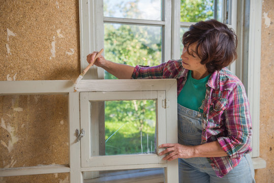 Mature Woman Is Painting An Old Window During Repair At Home