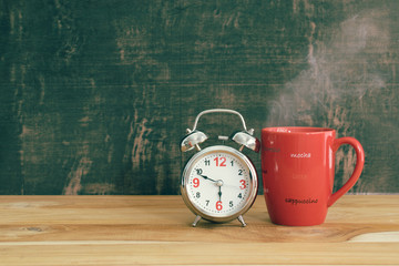 Retro alarm clock with red cup of cappuccino with blackboard bac