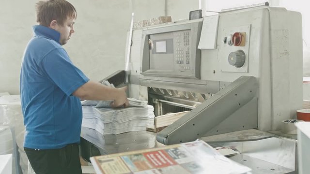 Worker in blue jacket worker puts the paper in the cutter guillotine machine in a printing factory, slider