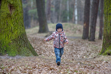 kid running in the outumn forest. Boy happy in fallen leaves to his mother