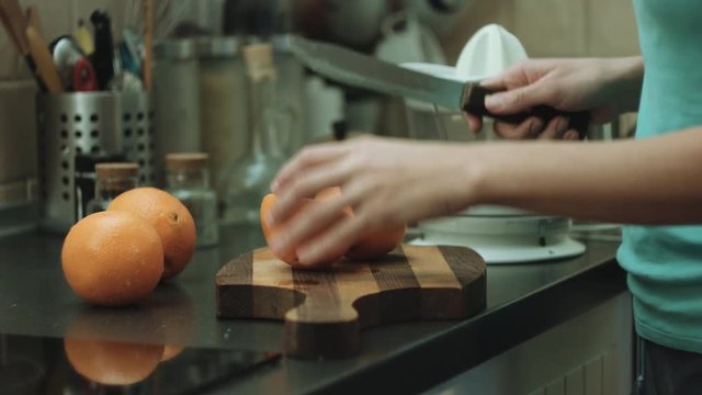 Close-up shot of the woman on kitchen cuts oranges on cutting board to make fresh juice in the juicer