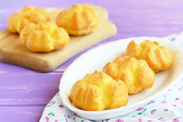 Delicious sweet eclairs or profiteroles with cream. Home made eclairs filled with butter cream on a plate and wooden cutting board. Closeup