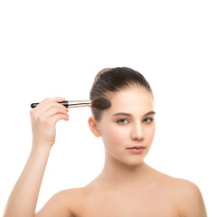 Fototapeta premium Portrait of beautiful young brunette woman with clean face. Beauty spa model girl with perfect fresh clean skin applying cosmetic brush. Youth and skin care concept. Isolated on a white background.