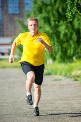 Running man jogging in city street park at beautiful summer day. Sport fitness model caucasian ethnicity training outdoor.