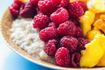 Organic oatmeal porridge in white ceramic bowl with raspberries, peaches and blueberries. Healthy breakfast - health and diet concept on the wooden table, close up.