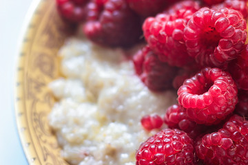 Organic oatmeal porridge in white ceramic bowl with raspberries, peaches and blueberries. Healthy breakfast - health and diet concept on the wooden table, close up.