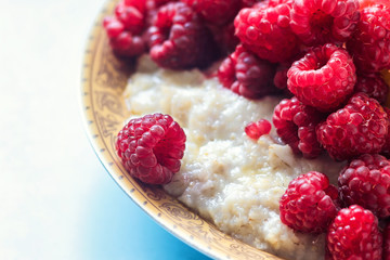 Organic oatmeal porridge in white ceramic bowl with raspberries, peaches and blueberries. Healthy breakfast - health and diet concept on the wooden table, close up.