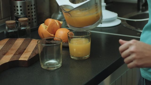 Woman in the kitchen pouring orange juice in two glasses