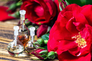 Obraz na płótnie Canvas Essential oil in glass bottle with red rose flowers and petals on wooden background. Beauty treatment. Spa and aromatherapy concept. Selective focus