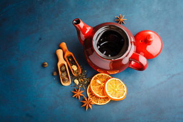 Teapot with dry tea over the blue background.
