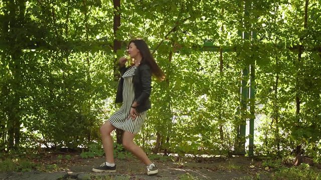 Beautiful brunette girl dancing at the grass wall in the park