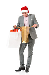 Caucasian man wearing christmas hat for santa. Young businessman in gray suit with shopping bags, isolated on white background. Successful boy wearing Santa Claus hat - full length portrait.