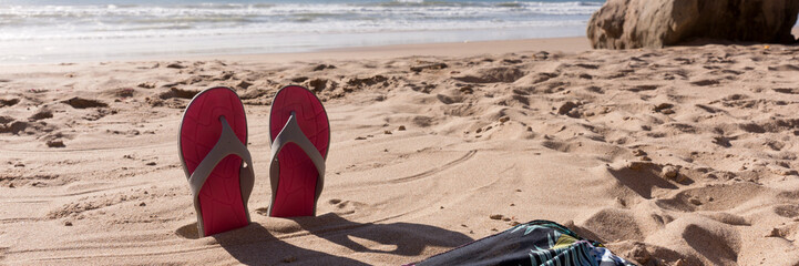 Travel background with a pair flip flops in the sand of a beach