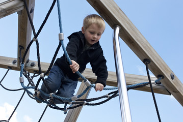 Little child blond boy climbing rope on the playground outdoors

