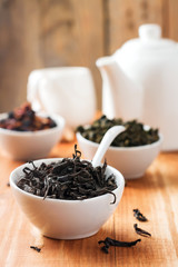 The black leaf tea in a white ceramic bowl on a wooden table. Selective focus.
