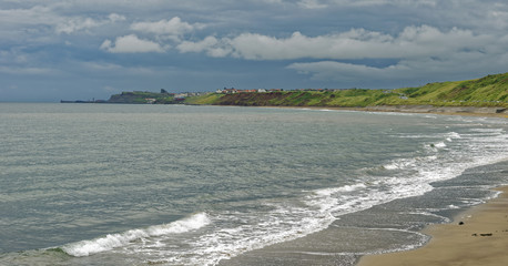 Beach view under a threatening sky of the coastline from Sandsend to Whitby in North Yorkshire, England