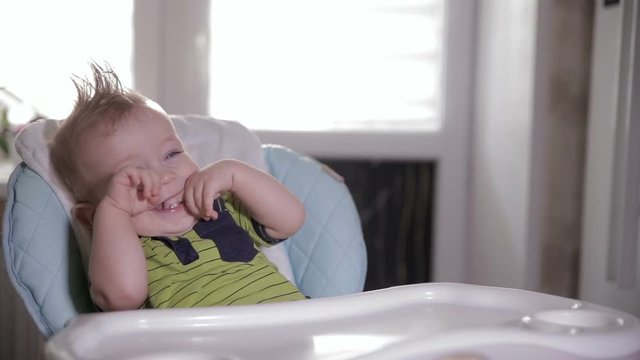 Cute shy baby in a baby chair laughing and looking into camera. HD.