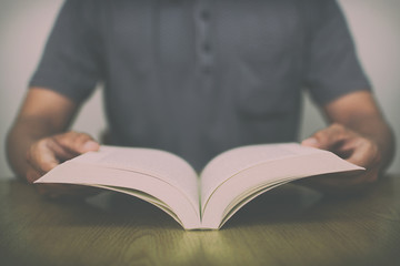 A man reading a book on wooden table with vintage filter blurred background