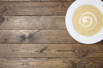 Fototapeta premium Aerial view of a bowl of hot chicken soup with swirl of cream on a rustic dining table background with blank space at side