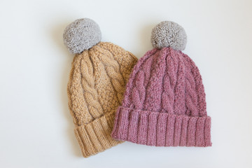 Two warm wool cap with pompon handmade beige and pink on a white table