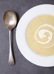 Aerial view of a bowl of hot chicken soup with swirl of cream on a dark slate background