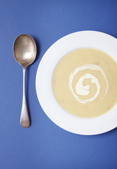 Overhead view of a bowl of hot chicken soup with swirl of cream on a blue background