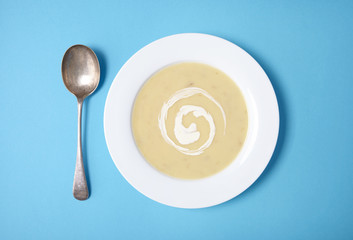 Aerial view of a bowl of hot chicken soup with swirl of cream on a bright blue background