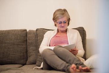 Senior woman with tablet sitting on couch in living room