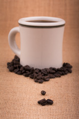 Coffee beans on burlap, with a coffee cup on background, with very light vignette