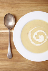 Aerial view of a bowl of hot chicken soup with swirl of cream on a wooden counter background